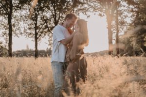 Zwangere dame met partner kussens met ondergaande zon in bloemenveld